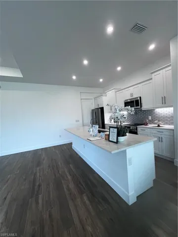 Kitchen island with light-toned countertop, dark wood-finish flooring, recessed lighting, and white cabinetry