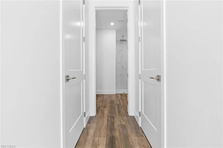 Hallway featuring wood-finish flooring, white paneled doors with brushed nickel hardware, and recessed lighting