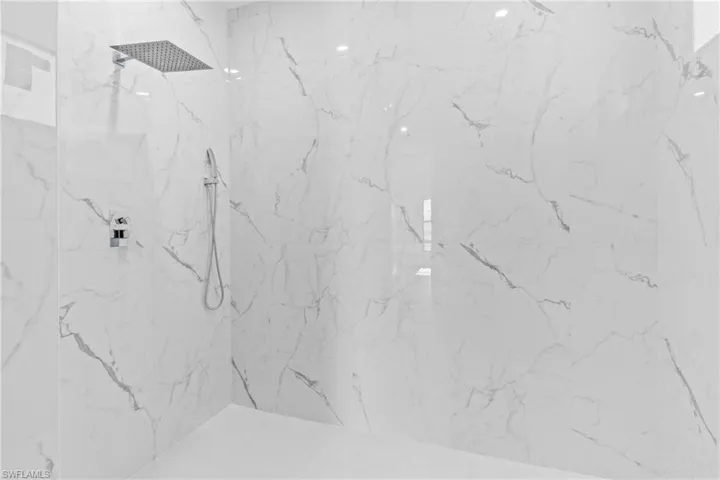 Walk-in shower with large-format white tile featuring grey veining, a rain showerhead, and a handheld shower fixture