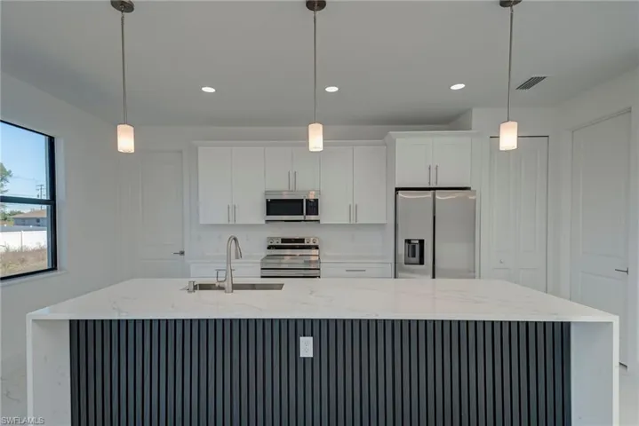 Kitchen with appliances with stainless steel finishes, light stone counters, white cabinets, decorative light fixtures, and recessed lighting