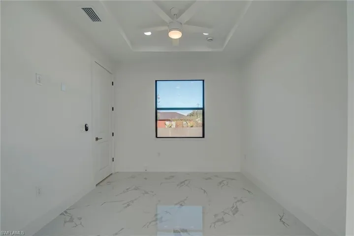 Empty room featuring marble tiled flooring, ceiling fan, and a raised ceiling