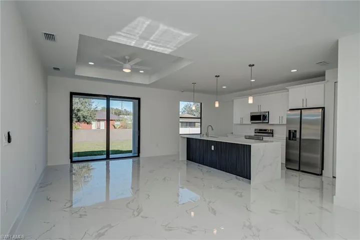 Kitchen with appliances with stainless steel finishes, a kitchen island with sink, open floor plan, pendant lighting, and light marble finish flooring