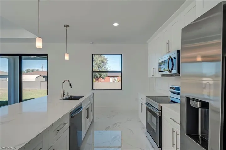 Kitchen featuring appliances with stainless steel finishes, white cabinets, pendant lighting, light marble finish floors, and recessed lighting