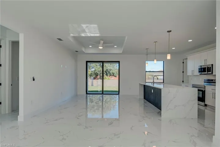 Kitchen with white cabinets, appliances with stainless steel finishes, pendant lighting, a raised ceiling, and light marble finish flooring