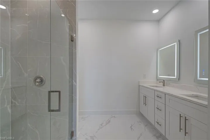 Bathroom with light marble finish flooring, double vanity, a marble finish shower, and recessed lighting
