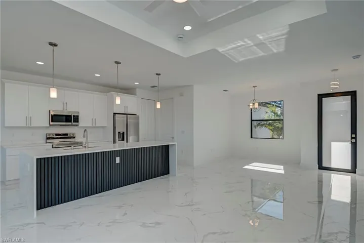 Kitchen featuring light marble finish floors, white cabinetry, hanging light fixtures, a large island with sink, and stainless steel appliances