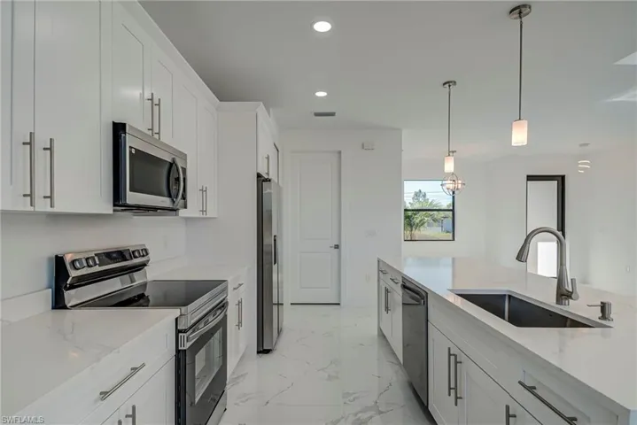Kitchen with appliances with stainless steel finishes, white cabinetry, light stone countertops, and recessed lighting