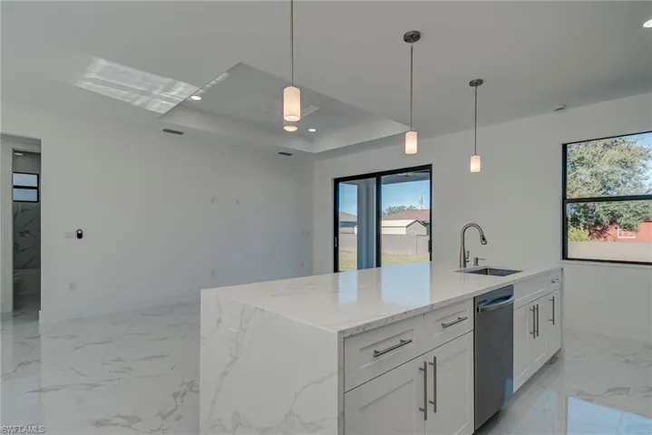 Kitchen featuring light marble finish floors, hanging light fixtures, a kitchen island with sink, light stone counters, and recessed lighting