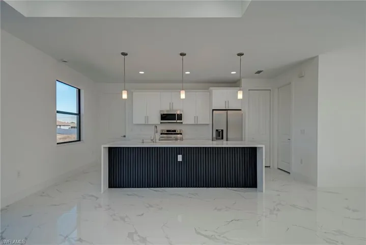 Kitchen with white cabinets, an island with sink, stainless steel appliances, light stone countertops, and hanging light fixtures
