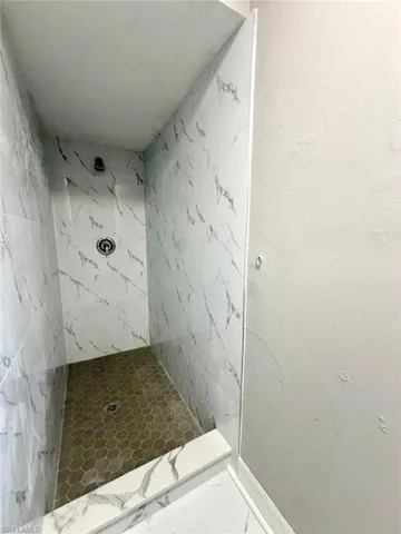 Full bath with a marble finish shower and baseboards