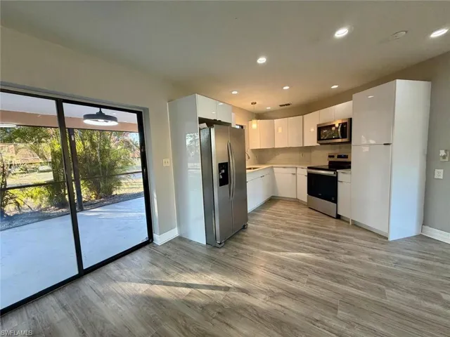 Kitchen with white cabinets, stainless steel appliances, hanging light fixtures, and modern cabinets