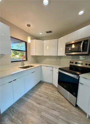 Kitchen with white cabinets, stainless steel appliances, modern cabinets, decorative light fixtures, and light wood finished floors