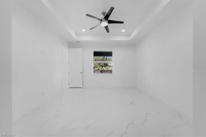 Spare room featuring light marble finish floors, a ceiling fan, recessed lighting, and a tray ceiling