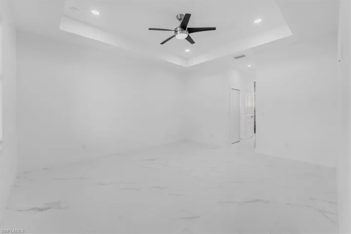 Unfurnished room featuring ceiling fan, light marble finish flooring, recessed lighting, and a raised ceiling