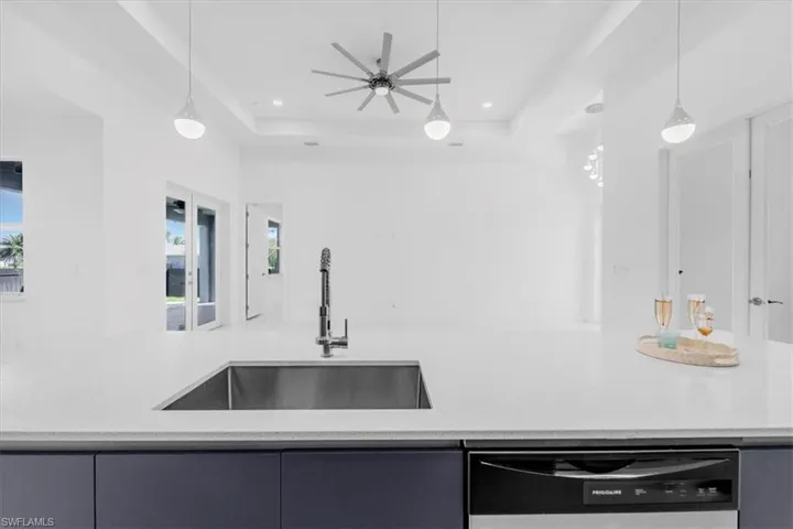 Kitchen featuring dishwasher, light stone countertops, a raised ceiling, and pendant lighting