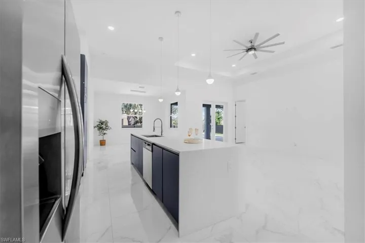 Kitchen featuring modern cabinets, stainless steel appliances, an island with sink, pendant lighting, and light stone counters
