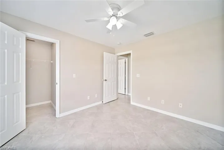 Neutral-toned room featuring large-format tile flooring, a white ceiling fan with integrated lighting, and multiple paneled doors providing access to closet and interior spaces