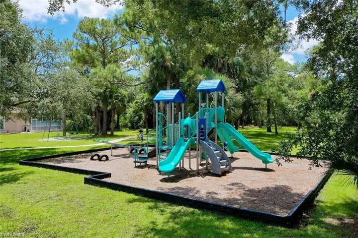 Outdoor recreation area featuring a multi-level structure with slides, stairs, and a balance beam, set within a mulched border and surrounded by mature landscaping