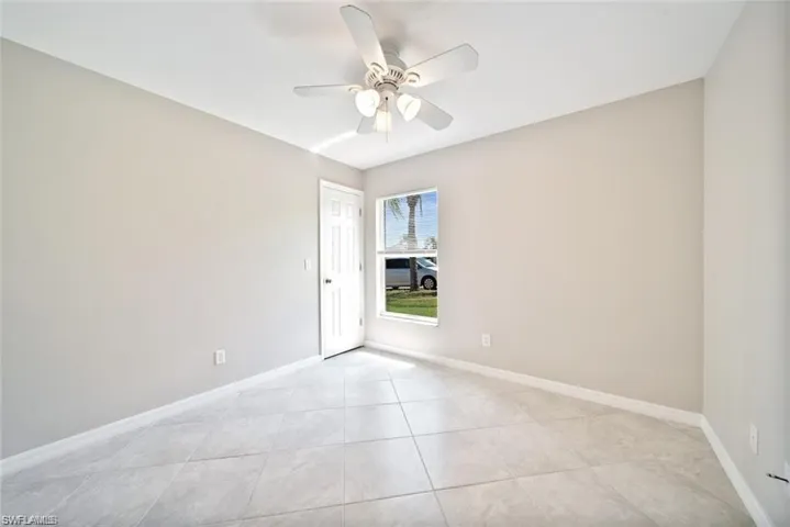 Neutral-toned interior featuring large-format tile flooring, a six-panel door, and a ceiling fan with integrated light fixture