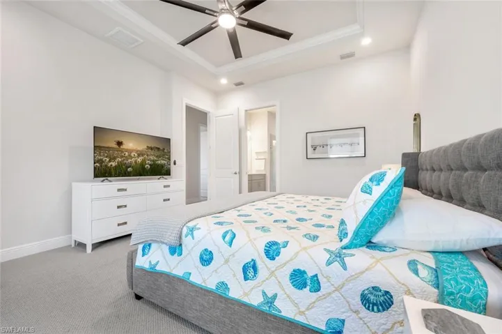 Bedroom with ceiling fan, a tray ceiling, carpet floors, and connected bathroom