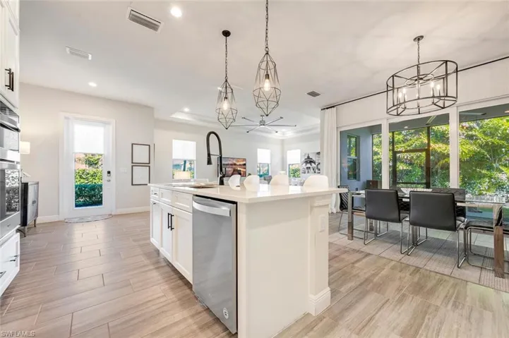 Kitchen featuring hanging light fixtures, an island with sink, dishwasher, and white cabinetry