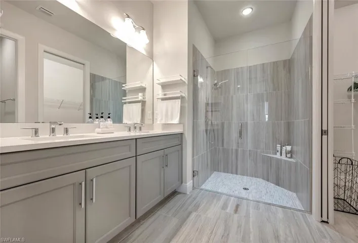 Primary ensuite bath featuring a tile shower, large vanity, tile floors, and double sink