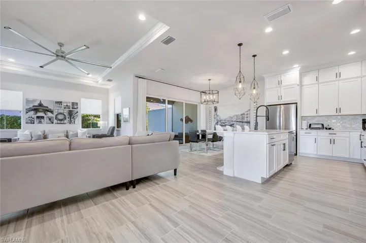 Living room featuring plenty of natural light, a tray ceiling, crown molding, and ceiling fan with notable chandelier