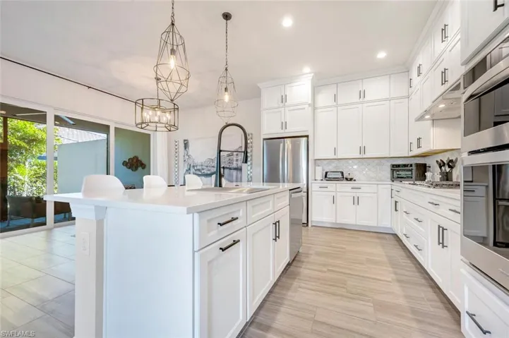 Kitchen with an island with sink, stainless steel appliances, backsplash, hanging light fixtures, and white cabinets