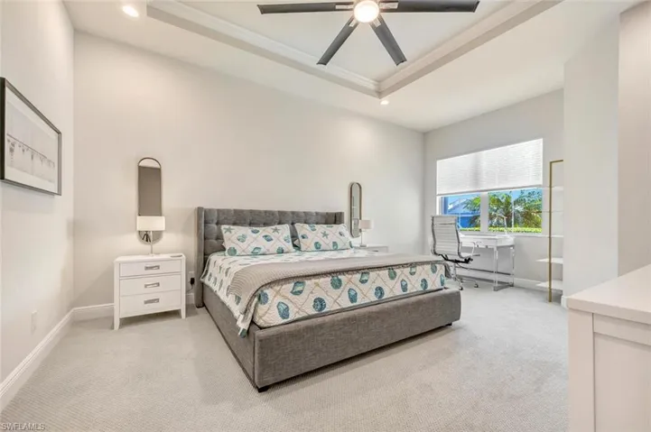 Carpeted bedroom with ceiling fan, a tray ceiling, and crown molding