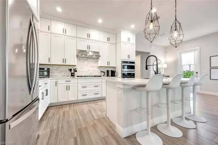 Kitchen featuring white cabinets, light hardwood / wood-style flooring, backsplash, a center island with sink, and appliances with stainless steel finishes