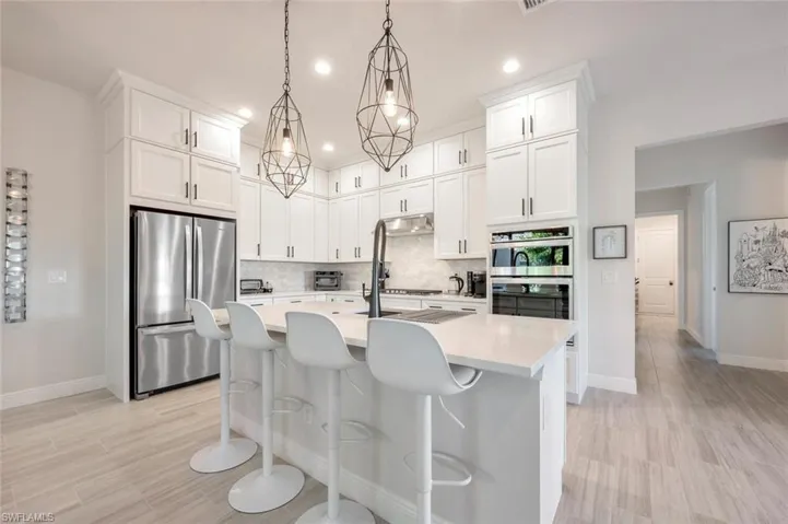 Kitchen featuring stainless steel appliances, backsplash, hanging light fixtures, a kitchen island with sink, and white cabinets