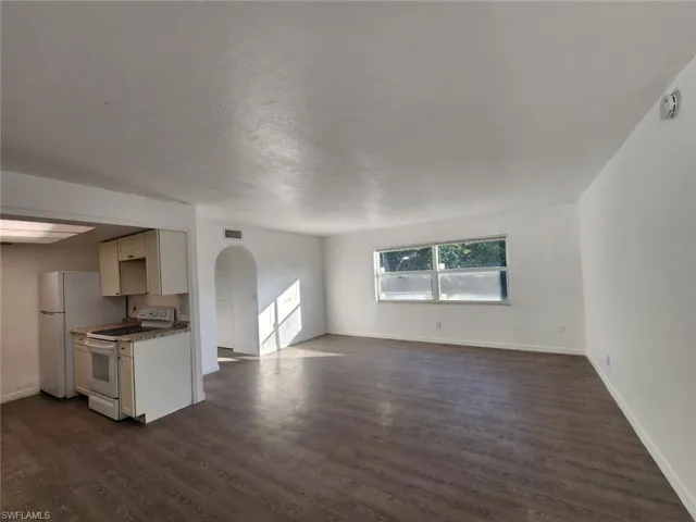 Unfurnished living room featuring arched walkways and dark wood-type flooring