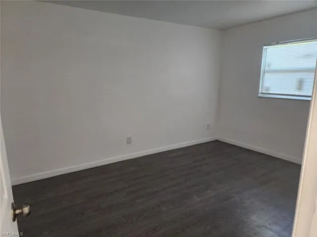 Unfurnished room featuring dark wood-style flooring and baseboards