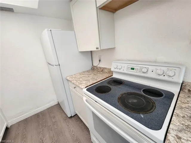 Kitchen featuring white appliances, white cabinetry, light countertops, light wood-style flooring, and a textured wall