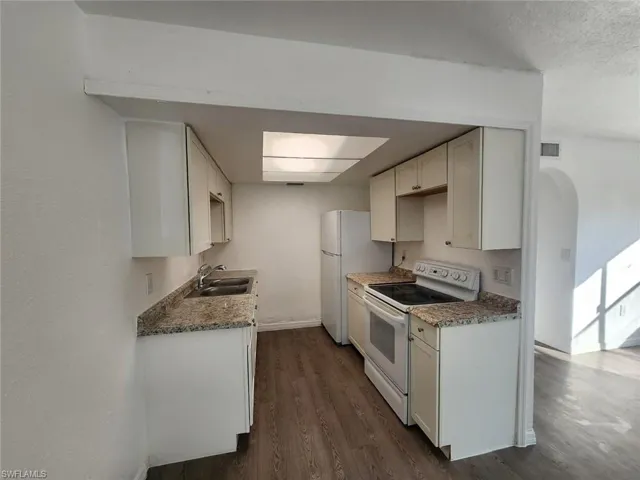 Kitchen featuring white appliances, dark wood-style floors, light countertops, arched walkways, and a textured ceiling