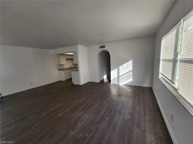 Unfurnished living room with arched walkways, dark wood-style flooring, and healthy amount of natural light