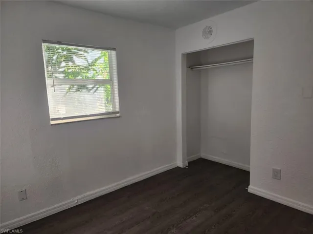 Unfurnished bedroom featuring dark wood finished floors, a textured wall, and a closet