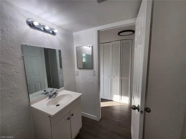 Bathroom with a textured wall, vanity, dark wood finished floors, a textured ceiling, and a closet