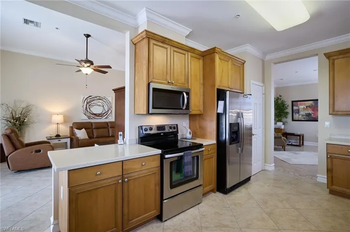 Kitchen featuring ornamental molding, appliances with stainless steel finishes, light tile patterned floors, and ceiling fan