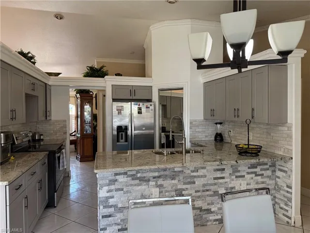 Kitchen featuring backsplash, gray cabinetry, appliances with stainless steel finishes, light tile patterned floors, and ornamental molding