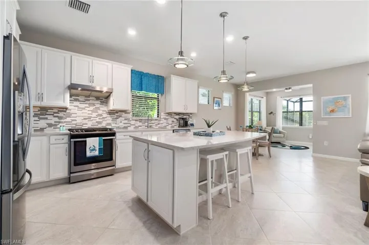 Kitchen featuring a breakfast bar area, pendant lighting, stainless steel appliances, a center island, and white cabinetry and quartz counters