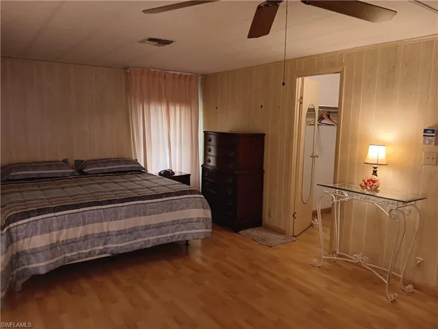Bedroom featuring wood finished floors, a walk in closet, wooden walls, and a ceiling fan