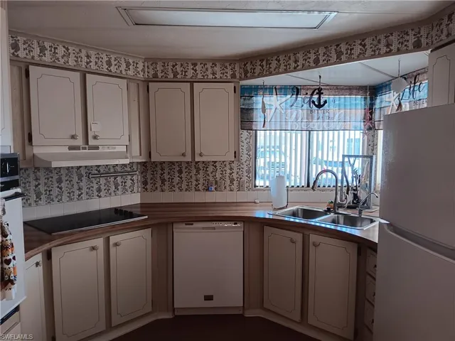 Kitchen with white appliances, white cabinetry, under cabinet range hood, and dark countertops
