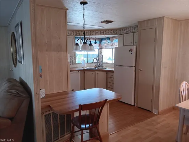 Kitchen featuring wood walls, white appliances, light wood-style flooring, hanging light fixtures, and light countertops