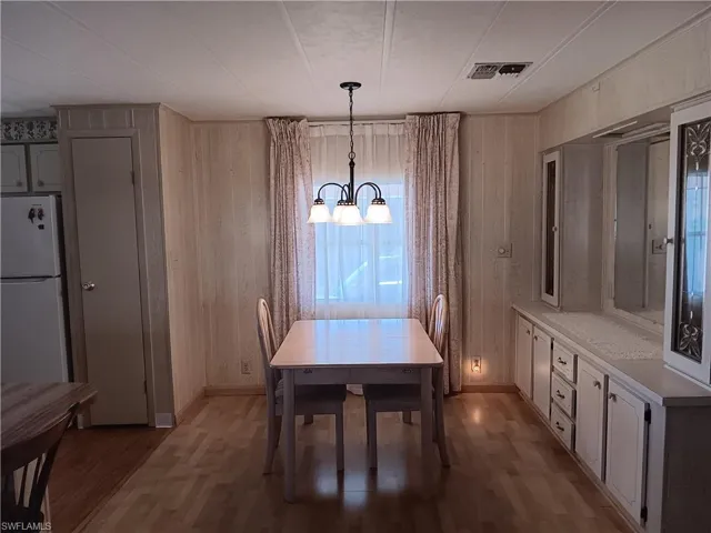 Dining space with dark wood finished floors, a chandelier, and wood walls