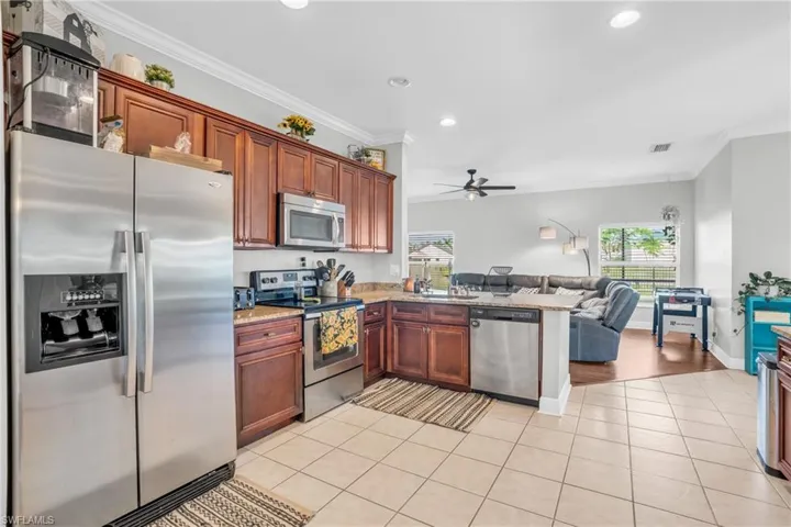 Kitchen featuring appliances with stainless steel finishes, kitchen peninsula, light hardwood / wood-style floors, ceiling fan, and ornamental molding