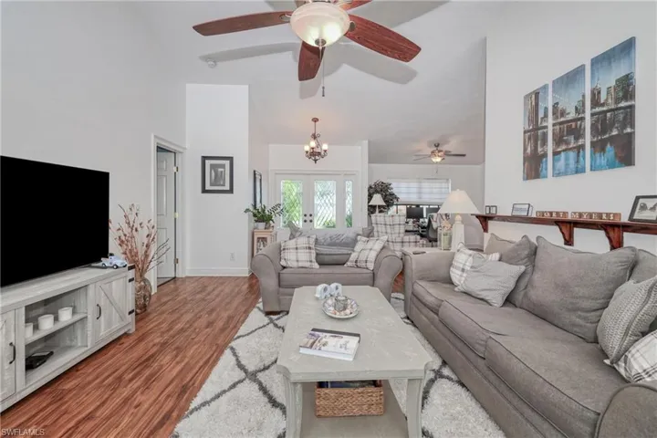 Living room featuring high vaulted ceiling, ceiling fan with notable chandelier, wood-type flooring, and french doors
