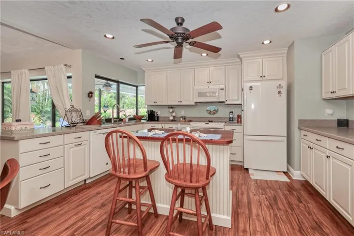 Kitchen featuring a kitchen breakfast bar, white appliances, a center island, and ceiling fan