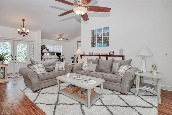Living room with ceiling fan with notable chandelier, vaulted ceiling, and light hardwood / wood-style floors