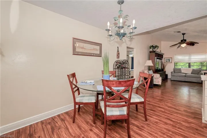 Dining area with a textured ceiling, ceiling fan with notable chandelier, and dark hardwood / wood-style flooring